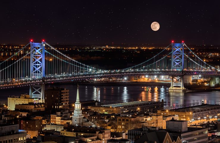 view of a full moon and ben franklin bridge at night